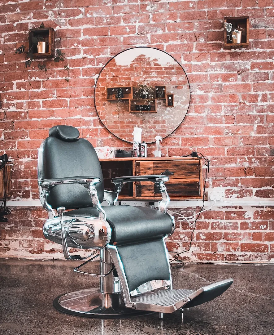 A single chrome barber chair with a round mirror against the full exposed-brick wall at Amunra Barbershop.