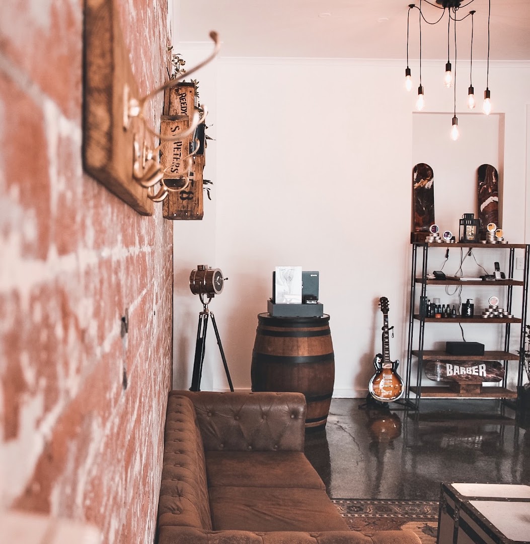 Inside Amunra Barbershop on Malvern Road — exposed brick wall, leather chesterfield, vintage barber chairs and warm Edison-bulb lighting