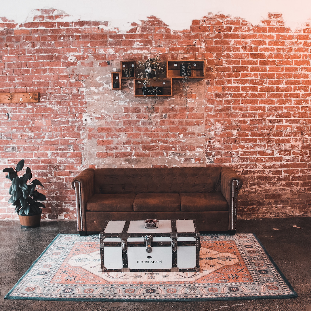 Original 1920s exposed brick wall behind the leather chesterfield and vintage steamer trunk at Amunra Barbershop