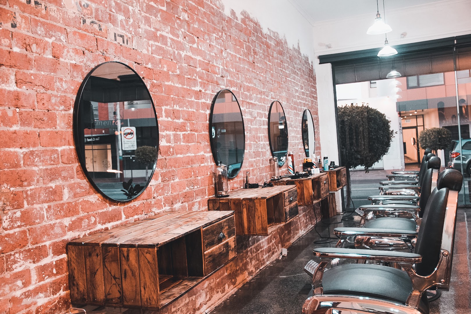 Looking through Amunra Barbershop's front window onto Malvern Road, Glen Iris, with round mirrors and chrome barber chairs along the brick wall
